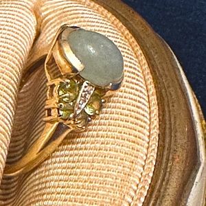 14k gold ring with green stones, clear stones, and a center smooth type stone.